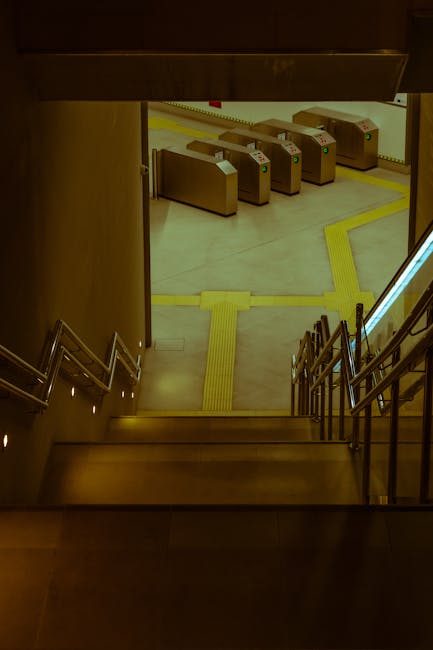 View from the top of a staircase looking down into a station entrance area at Hither Green, featuring a set of four automatic ticket barriers made of beige plastic with card readers and indicator ligh
