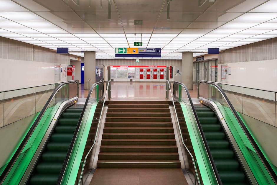 View from the top of a staircase looking down into a station entrance area at Hither Green, featuring a set of four automatic ticket barriers made of beige plastic with card readers and indicator ligh